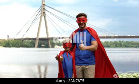 Vater und Sohn in Superhelden kostüme zeigen Daumen oben, Motivation und Teamarbeit Stockfoto
