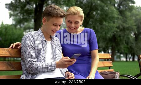Sohn und Mutter sitzt auf der bank Sehen Smartphone Fotos beim Spaziergang getroffen Stockfoto