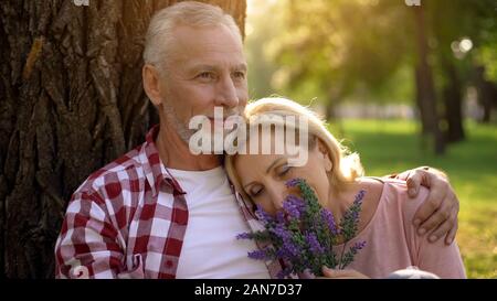 Alte Frau liegen auf mans Schulter, Senior Paar sitzt im Park in der Nähe von Tree, Datum Stockfoto