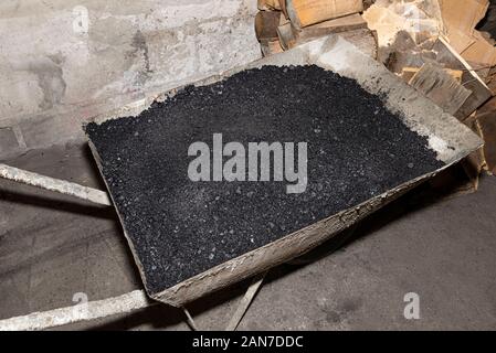 Schubkarre Beladen mit Kohle im Kesselhaus neben dem Ofen und Brennholz. Stockfoto