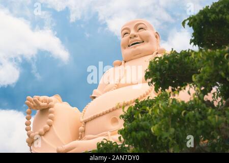 Lachender Buddha Statue an Vinh Trang Tempel, in der Nähe von My Tho, Vietnam. Low Angle View mit Baum im Vordergrund. Stockfoto