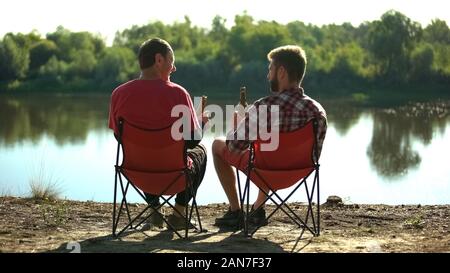Freunde aus der Kindheit sitzen am Flussufer, trinken Bier und Diskutieren, Angeln Stockfoto