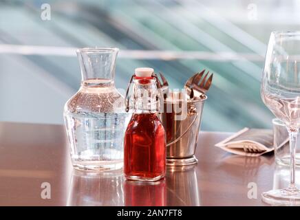 Eine Karaffe Wasser, eine Flasche roten Trauben Essig und eine Bronze Eimer mit Besteck auf die glatte Spiegelfläche von einem Tisch in ein Fischmarkt in Frankreich Stockfoto