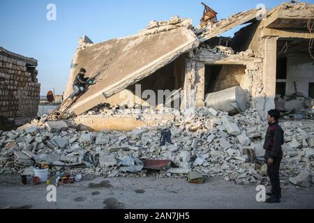 Kafr Nabl, Syrien. 14 Jan, 2020. Ein Bild am 16. Januar 2020 zur Verfügung gestellt zeigt eine Syrische boy watching syrischen Künstler Abu Malik Al-Shami (L) während des Zeichnens einer Graffiti Wandbild an der Wand eines Gebäudes, die in einem Luftangriff zerstört wurde. Al-Shami gestartet Malerei Wandbilder zurück in 2014 an den Wänden der zerstörten Gebäude seiner dann belagerte Home - Stadt Darayya, gelegen im Süden westlich von Damaskus. Nach seiner Vertreibung, der Künstler weiter Wandbilder in Idlib zu malen, die Aufmerksamkeit auf die verheerende humanitäre Lage zu zeichnen. Credit: Anas Alkharboutli/dpa/Alamy leben Nachrichten Stockfoto