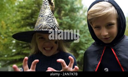 Mädchen in Hexenhut und Junge in Mantel jagen Kamera, Knurren, Spooky, Halloween Stockfoto