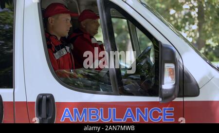 Männliche Sanitäter in Krankenwagen sitzen, bereit, auf Abruf zu fahren, Fachleute Stockfoto