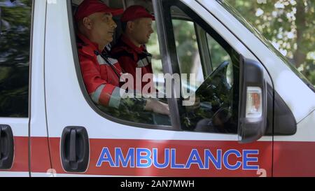 Männliche Ärzte in Krankenwagen sitzen, bereit, auf Abruf zu fahren, Fachleute Stockfoto