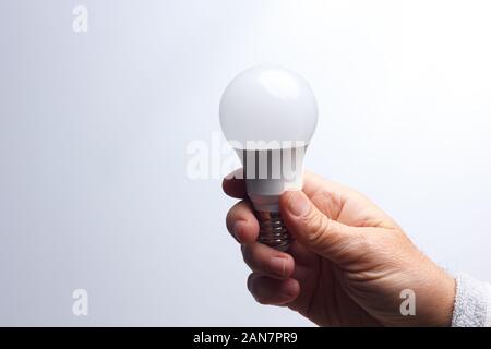 Tageslicht Energiesparbirne, in der Hand eines Erwachsenen; Lampe bereit, installiert und an das Stromnetz angeschlossen werden; es gibt Licht und wenig Wärme. Stockfoto