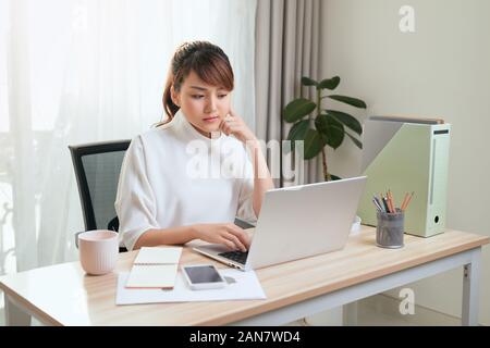 Junge Asiatische schöne Frau arbeitet für einen Computer von einem Haus mit einem Laptop auf dem Schreibtisch als Freiberufler Stockfoto