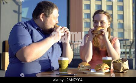 Pralle Mann und Frau essen Burger und Pommes frites, Kollegen vor dem Mittagessen Stockfoto