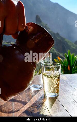 Man gießt Weißwein aus Ton Kanne in Glas auf der Terrasse in sunlights mit Blick auf die grüne Landschaft der kleinen Bergdorf Masca auf Teneriffa, Spa Stockfoto