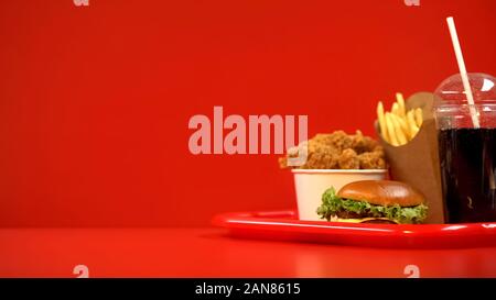 Gebratene Flügel Pommes frites Hamburger und Soda Drink auf rot Fach, Essen zum Mitnehmen Stockfoto