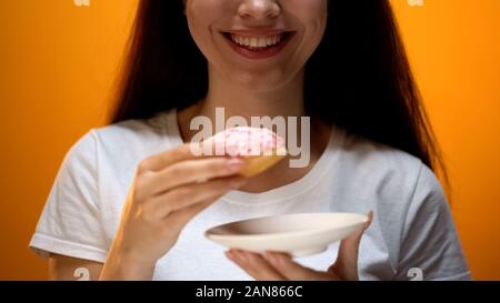 Girl holding Donut, lächelnd auf Kamera, Neigung zu süße Nahrungsmittel, Diabetes Risiko Stockfoto