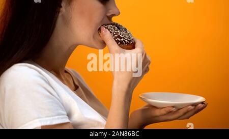 Mädchen beißen Schokolade Donut, hochkalorische süße Speisen, erhöhter Blutzucker Diabetes Stockfoto