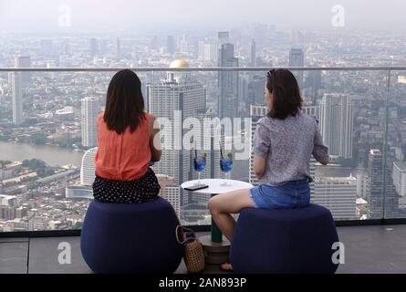 Zwei Frauen sitzen auf dem Dach der King Power MahaNakhon Gebäude mit blauen Getränke auf den Tisch und beobachtete Bangkok Stadtbild. Stockfoto