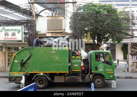 Bangkok, Thailand - 26. Dezember 2019: Grüne Müllwagen. Ein Arbeiter sitzen auf dem Dach mit vielen schwarzen Plastiktüten. Stockfoto