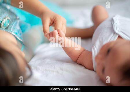 Neugeborenes Baby mit ihrer älteren Schwester zusammen auf dem Bett halten einander die Hand Stockfoto