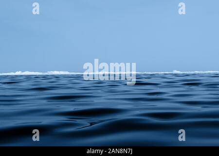 Hintergrund Textur des blauen Wellenlinien Eis des Baikalsees mit Hängematten am Horizont und blauer Himmel. Stockfoto