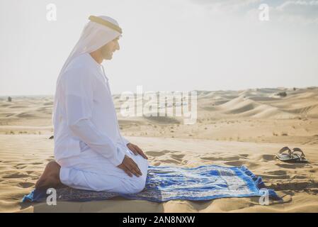 Mann mit weissen Traditionelle kandura von uae betend in der Wüste auf dem Teppich Stockfoto