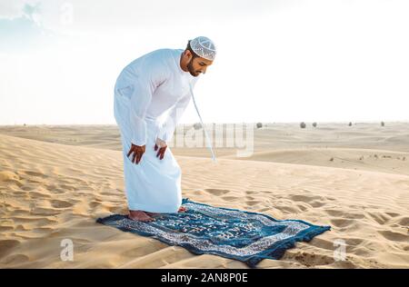 Mann mit weissen Traditionelle kandura von uae betend in der Wüste auf dem Teppich Stockfoto