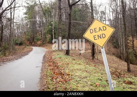 Eine leere Landstraße hinauf in den Wald mit einer Sackgasse Zeichen gebogen in einem Winkel an einem trüben Tag. Stockfoto