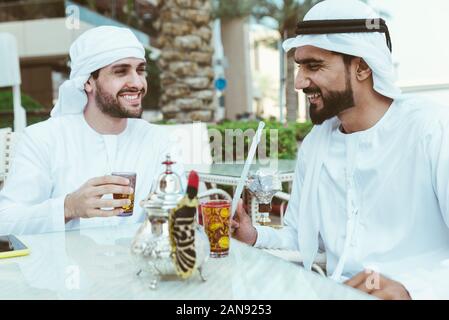 Zwei junge Unternehmer Ausgehen in Dubai. Freunde tragen Der kandura traditionelle männliche Outfit in Marina Stockfoto