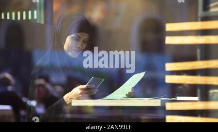 Schönen muslimischen Frau Freelancer im Cafe Arbeiten, Chatten mit Partner auf Telefon Stockfoto