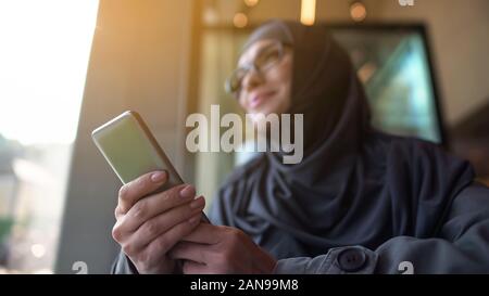 Fröhliche muslimischen Frau Telefon in der Hand, nach außen durch Fenster Cafe Stockfoto