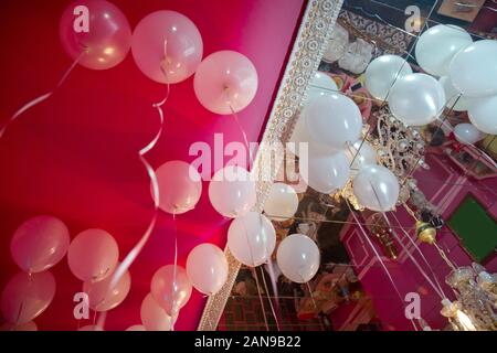 Hochzeit oder Kindergeburtstag Dekoration Interieur. Helium Luftballons rot schweben. weiße Ballons auf die weiße Decke im Zimmer Hin- und Herbewegung für die Stockfoto