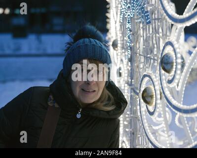 Eine glückliche Frau im Winter Kleidung in der Nähe von Weihnachten Beleuchtung Posing, Nacht Stockfoto