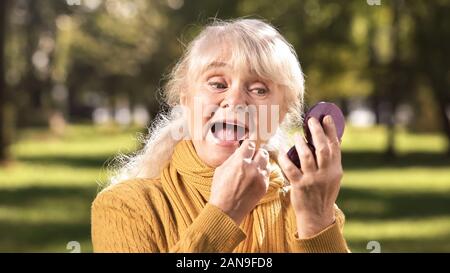 Gerne alte Dame mit Lippenstift, sitzt auf der Bank im Park, Anti-Age-Kosmetik Stockfoto