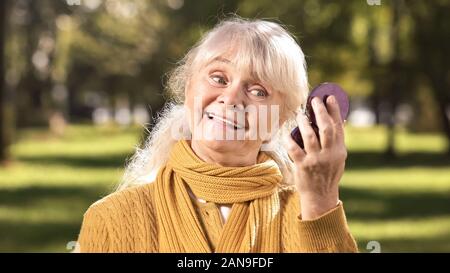 Freundliche alte Frau aufrichtig lächelte ihr Spiegelbild in kompakten Spiegel Stockfoto