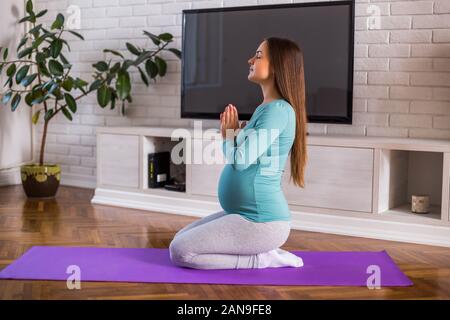 Schöne schwangere Frau genießt Ausübung von Yoga an ihrem Haus. Stockfoto