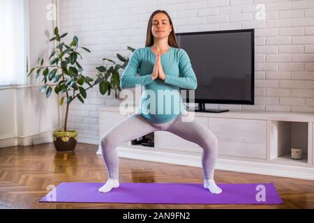 Schöne schwangere Frau genießt Ausübung von Yoga an ihrem Haus. Stockfoto