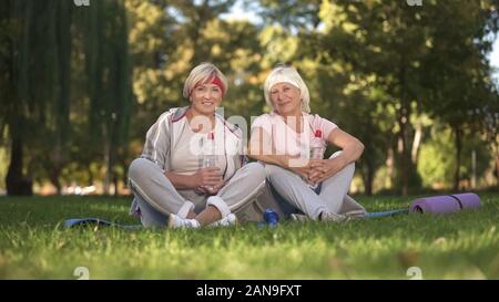 Zwei Frauen sitzen auf Gras und lächelnd in die Kamera nach dem Yoga Stockfoto