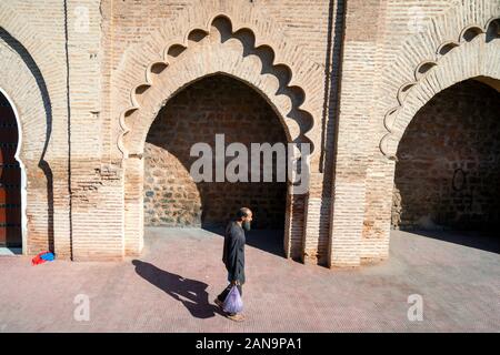 Marrakesch, Marokko - Januar 7, 2020: Mann mit Einkaufsmöglichkeiten zu Fuß entlang der alten Moschee Wand Stockfoto