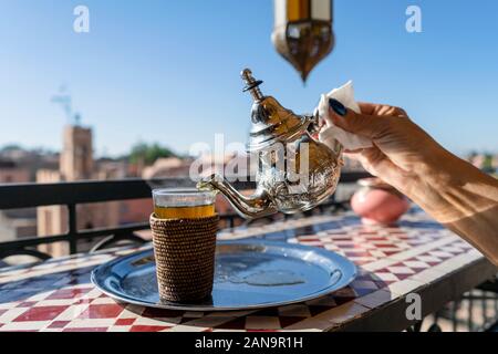 Gießen marokkanischen Tee aus Silber, Wasserkocher auf dem Glas auf dem Dach von Marrakesch, Marokko Stockfoto