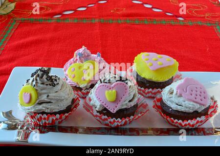 Liebe Muffins, bunten Cupcakes mit Marzipan Herzen aus weisser Keramik Untertasse serviert dekoriert, Seitenansicht Stockfoto