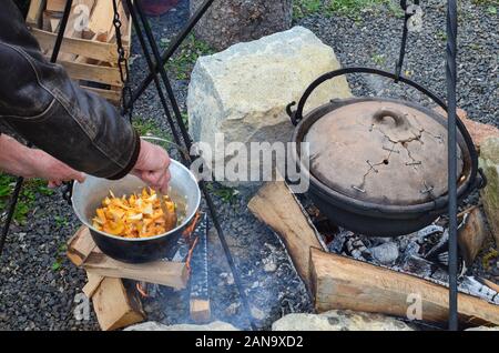 Vorbereitung Pilze und Wildbret Gulasch auf offenem Feuer in einem Wasserkocher, Blending gehackte Zwiebel Chanterelle durch hölzerne Löffel Stockfoto