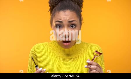 Überrascht afro-amerikanische Frau, die in der Kamera mit der Wimpernzange und Mascara Stockfoto