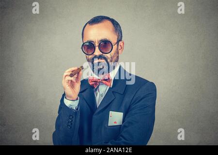 Ace card unter Hülse - Geschäftsmann. Ernsthafte bärtigen boss Sonnenbrille, eine Zigarre in der Hand mit Ace in seiner Tasche auf grauem Hintergrund. Stockfoto