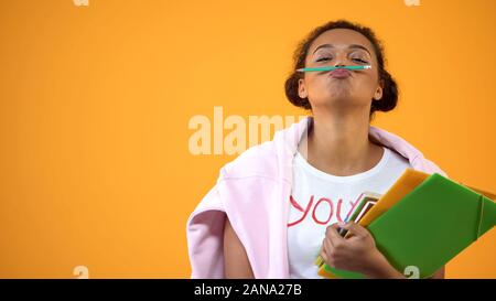 Positive afrikanische Teenager halten Bleistift zwischen Nase und Lippen, Schnurrbart Witz Stockfoto