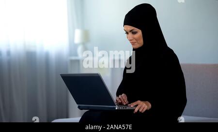 Muslimische Frau scrollen Laptop, zu Hause arbeiten, online Bildung, Technologie Stockfoto