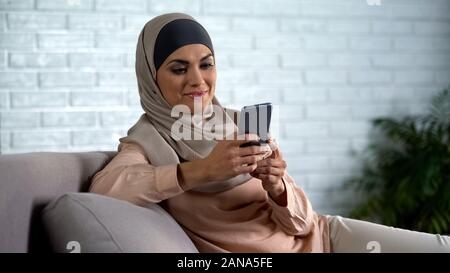 Lächelnd muslimische Frau zu Hause verwenden Smartphone, Chatten in sozialen Medien Stockfoto
