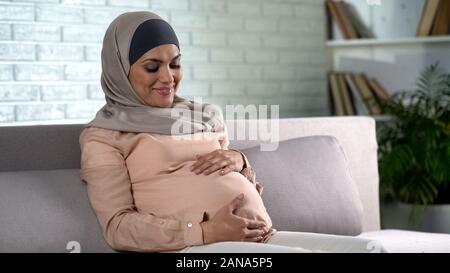 Lächelnd schwangere Frau im hijab Holding Bauch, baby Erwartung, Mutterschaft Stockfoto