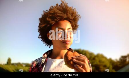Cute curly behaarte Frau genießen leckere Burger im Freien, fat Snacks und Fast Food Stockfoto