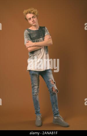 Studio shot von Skinny junger Mann mit lockigem Haar gegen braunen Hintergrund Stockfoto