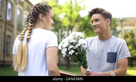 Teen boy präsentiert Feldblumen zu jugendlich Mädchen, lesen Buchen Sie im City Garden Stockfoto