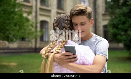 Teenager mit Handy während umarmen Freundin, durch soziale Netzwerke aufgenommen Stockfoto