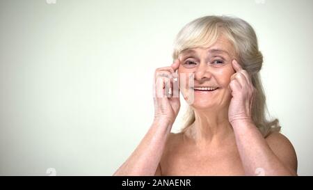 Attraktive alte Dame, Gesichts Übungen, anti-aging facebuilding Für die Augen Stockfoto